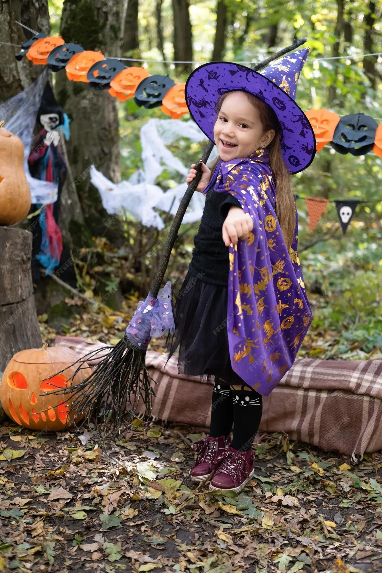 Niña feliz en disfraz de halloween y sombrero de bruja con escoba en  decoración de halloween al aire libre | Foto Premium