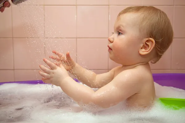 pequeña niña lava en una bañera de bebé con agua pulverizada y ...