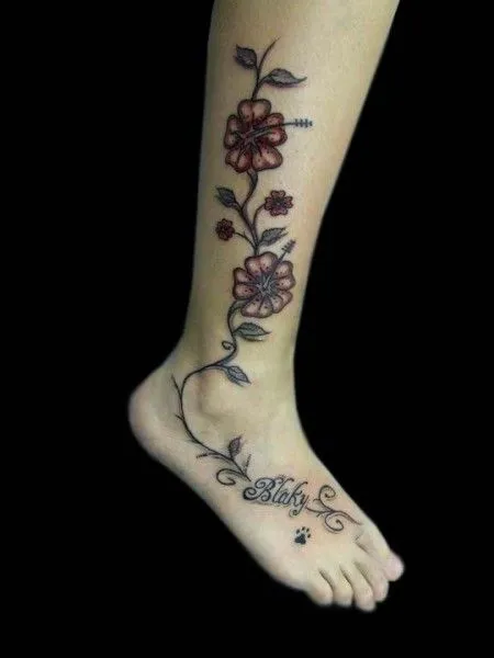 TATUAJE DE UNAS FLORES EN LA PIERNA CON UN NOMBRE Y UNA HUELLA